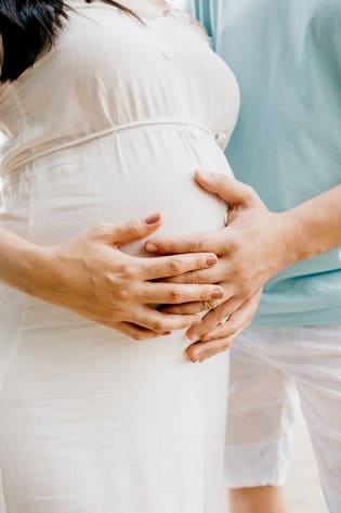 photo ronde d'une femme enceinte avec ses mains et celle du papa sur son ventre